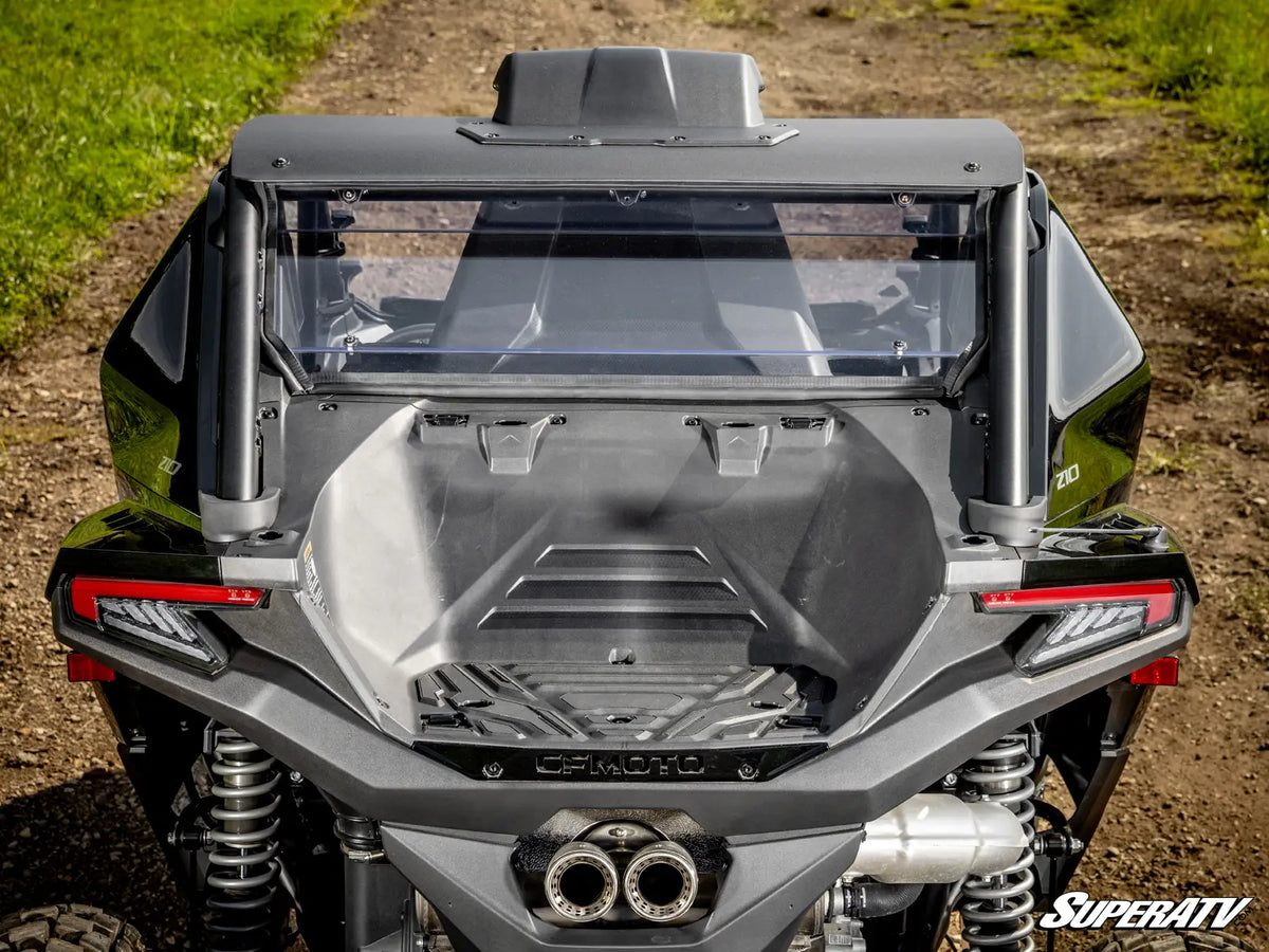 Rear view of a black Can-Am side-by-side UTV with a clear windshield and roll bar, parked on a dirt path with grass on both sides.