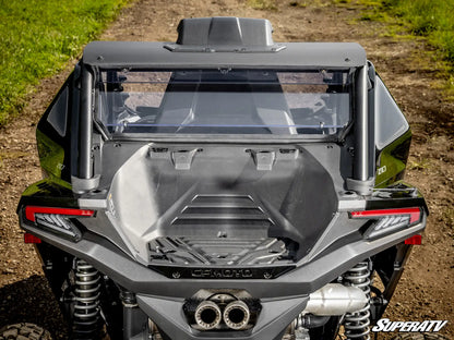 Rear view of a black Can-Am side-by-side UTV with a clear windshield and roll bar, parked on a dirt path with grass on both sides.