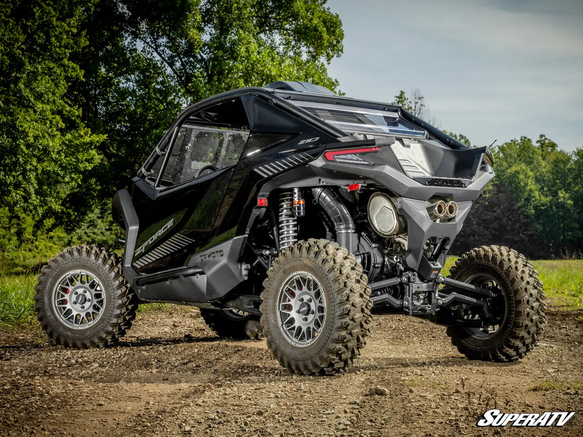 A black Can-Am side-by-side UTV with large off-road tires, shown from a three-quarter rear angle on a dirt path with trees in the background. A 'SUPERATV' watermark is visible in the bottom right corner.