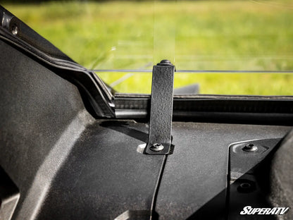 Close-up of a black metal mounting bracket installed on the dashboard of a vehicle, with a blurred green outdoor background visible through the windshield. The SuperATV logo is visible in the bottom right corner.
