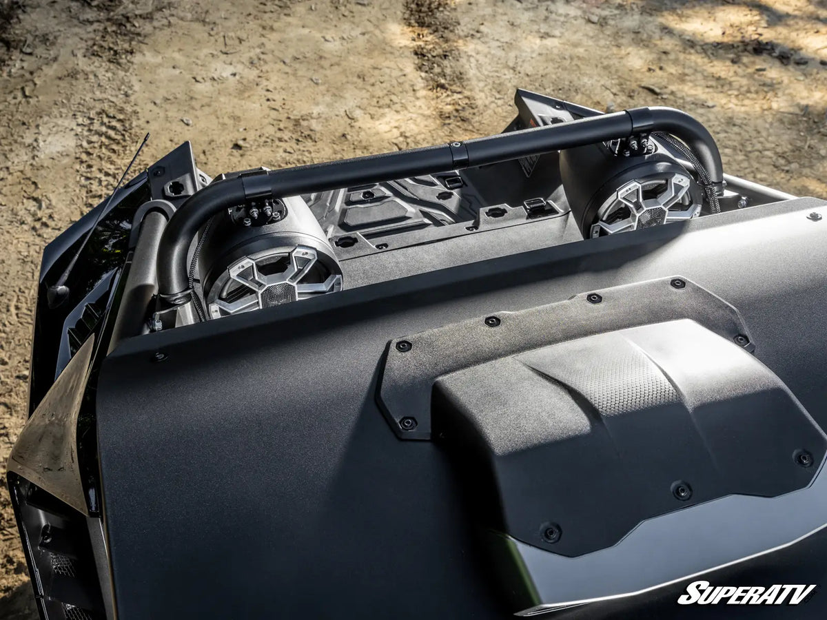 Close-up of a black off-road vehicle roll bar and hood details, with a SuperATV logo visible on the lower right, set against a dirt ground background.