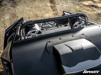 Close-up of a black off-road vehicle roll bar and hood details, with a SuperATV logo visible on the lower right, set against a dirt ground background.