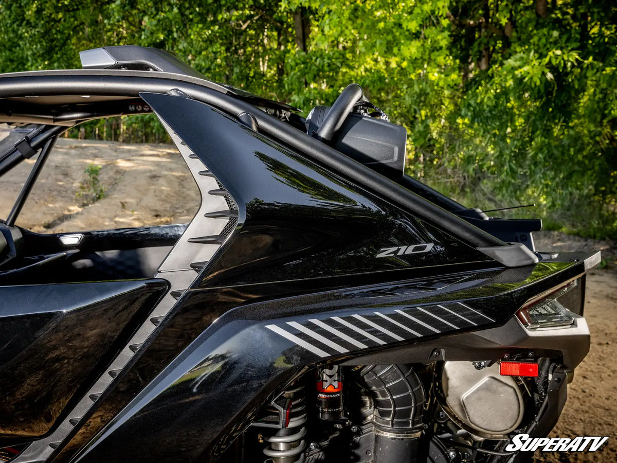 Close-up of a black Polaris ZIO R side-by-side vehicle with its roll cage and engine components visible, set outdoors against a background of green trees and dirt path. A SuperATV logo is visible in the bottom right corner.