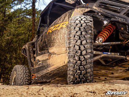 Off-road vehicle with large tires on a dirt path, featuring SuperATV branding.