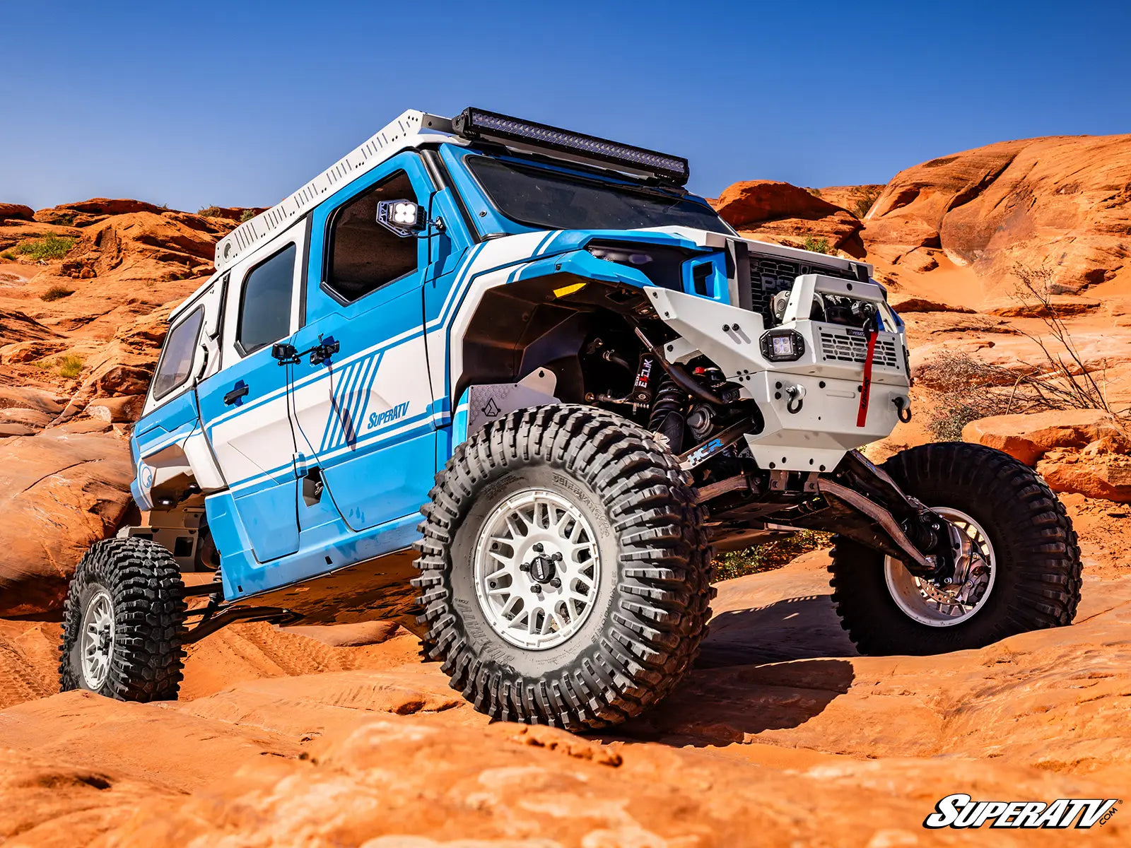 Blue and white off-road vehicle with large tires in a desert landscape, featuring SuperATV branding.