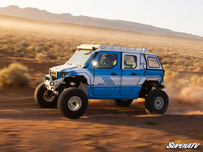 Blue off-road vehicle driving on a desert road with mountains in the background