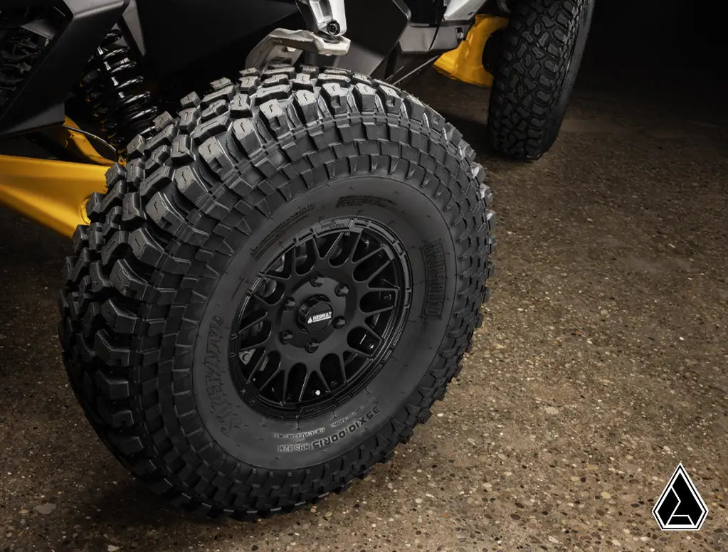 Close-up of a black off-road tire with tread pattern on a vehicle, on a dark surface.