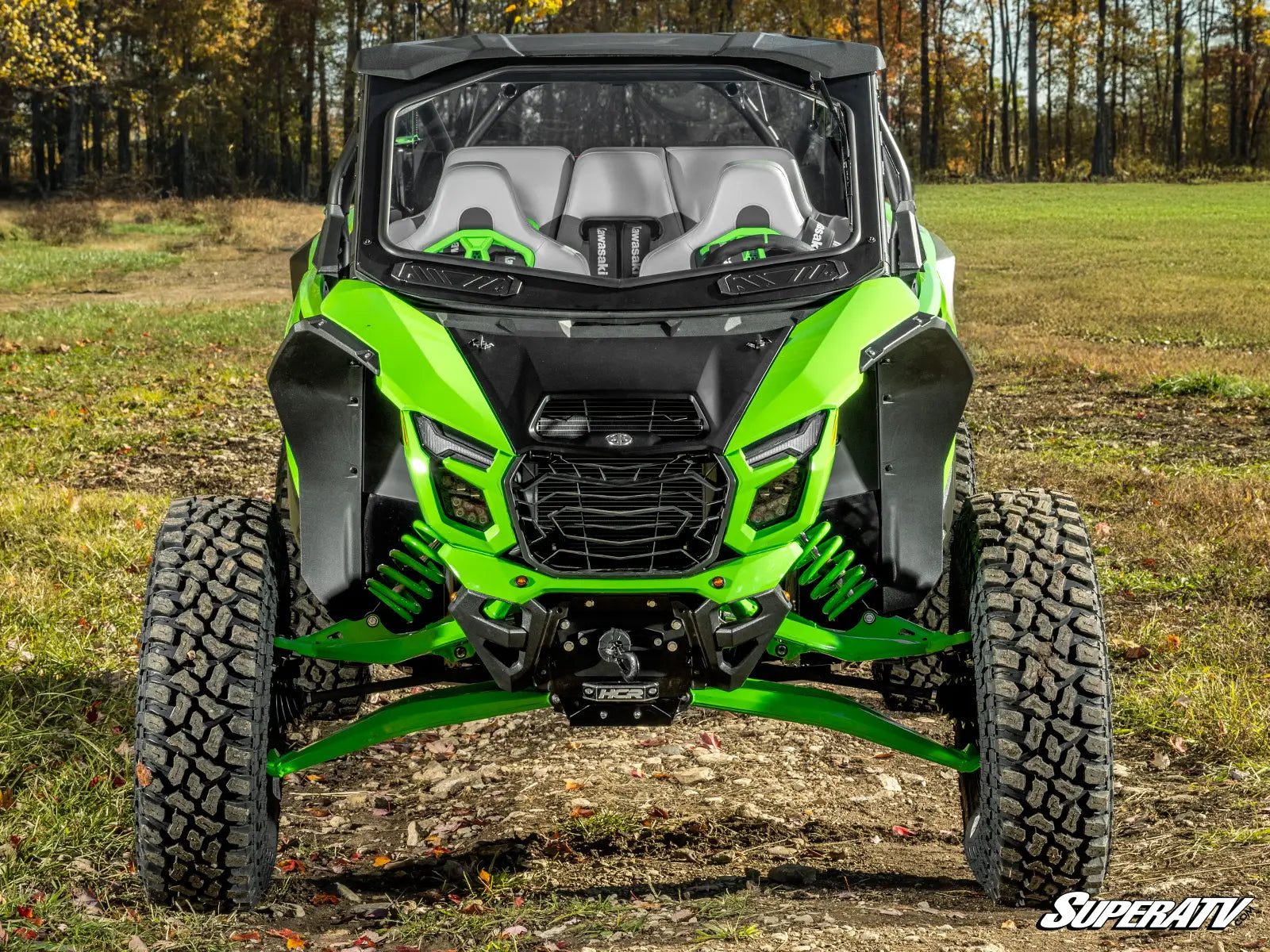 Green and black SuperATV vehicle in a field with trees in the background