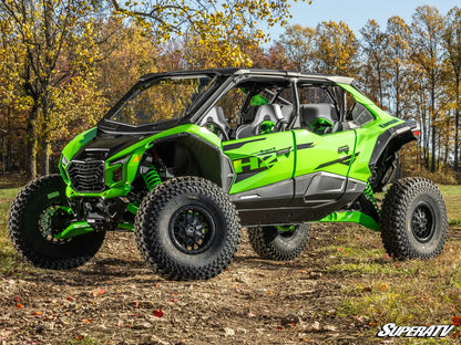 Green and black off-road vehicle on a dirt path with trees in the background