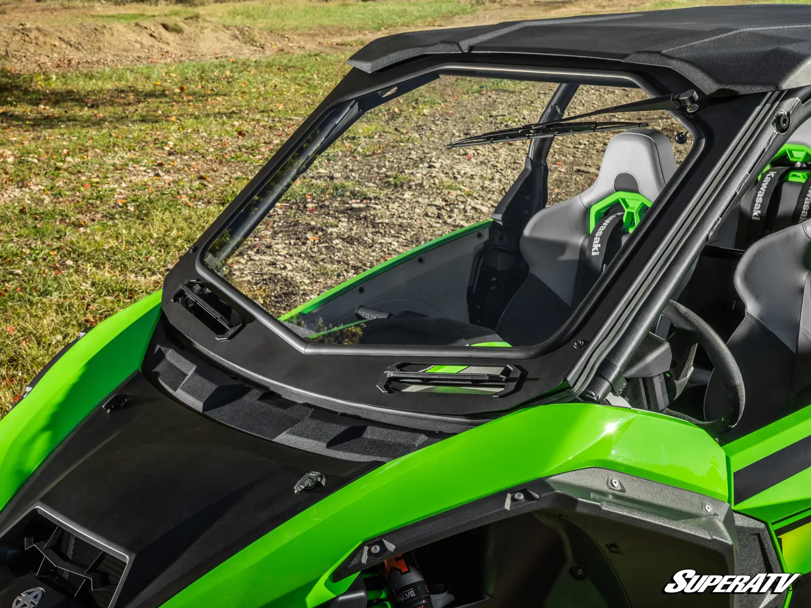 Green and black SuperATV vehicle with a clear windshield on a grassy background