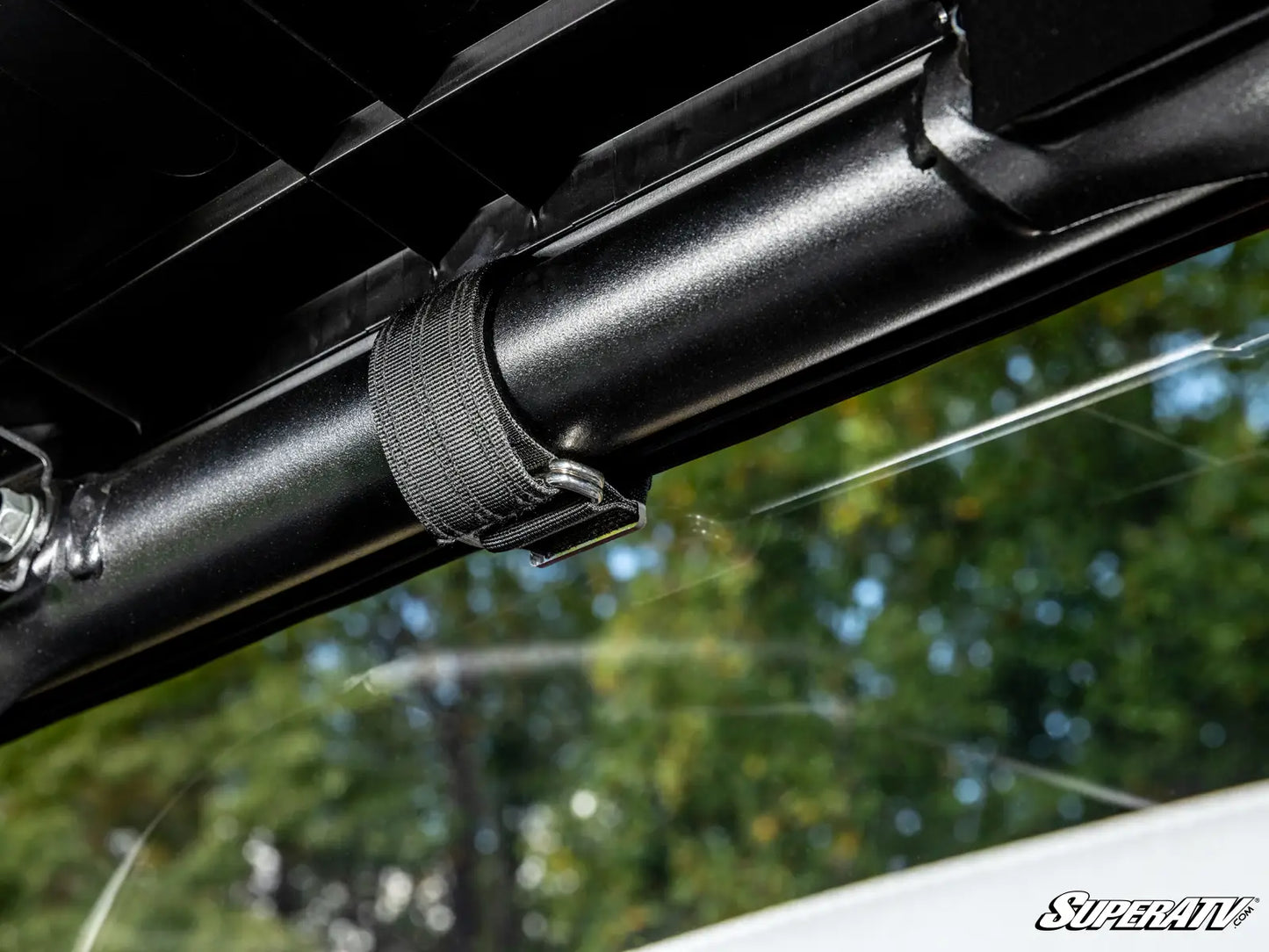 Close-up of a black metal bar with a strap, against a blurred natural background.