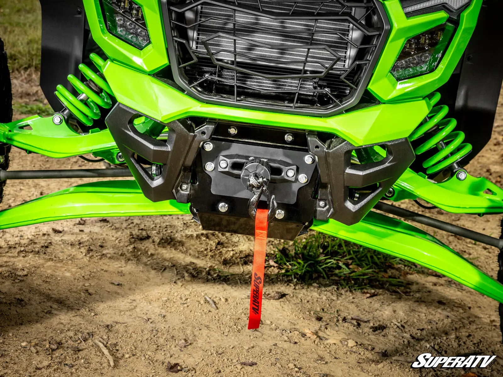 Close-up of a green ATV with a SuperATV logo on a dirt surface.