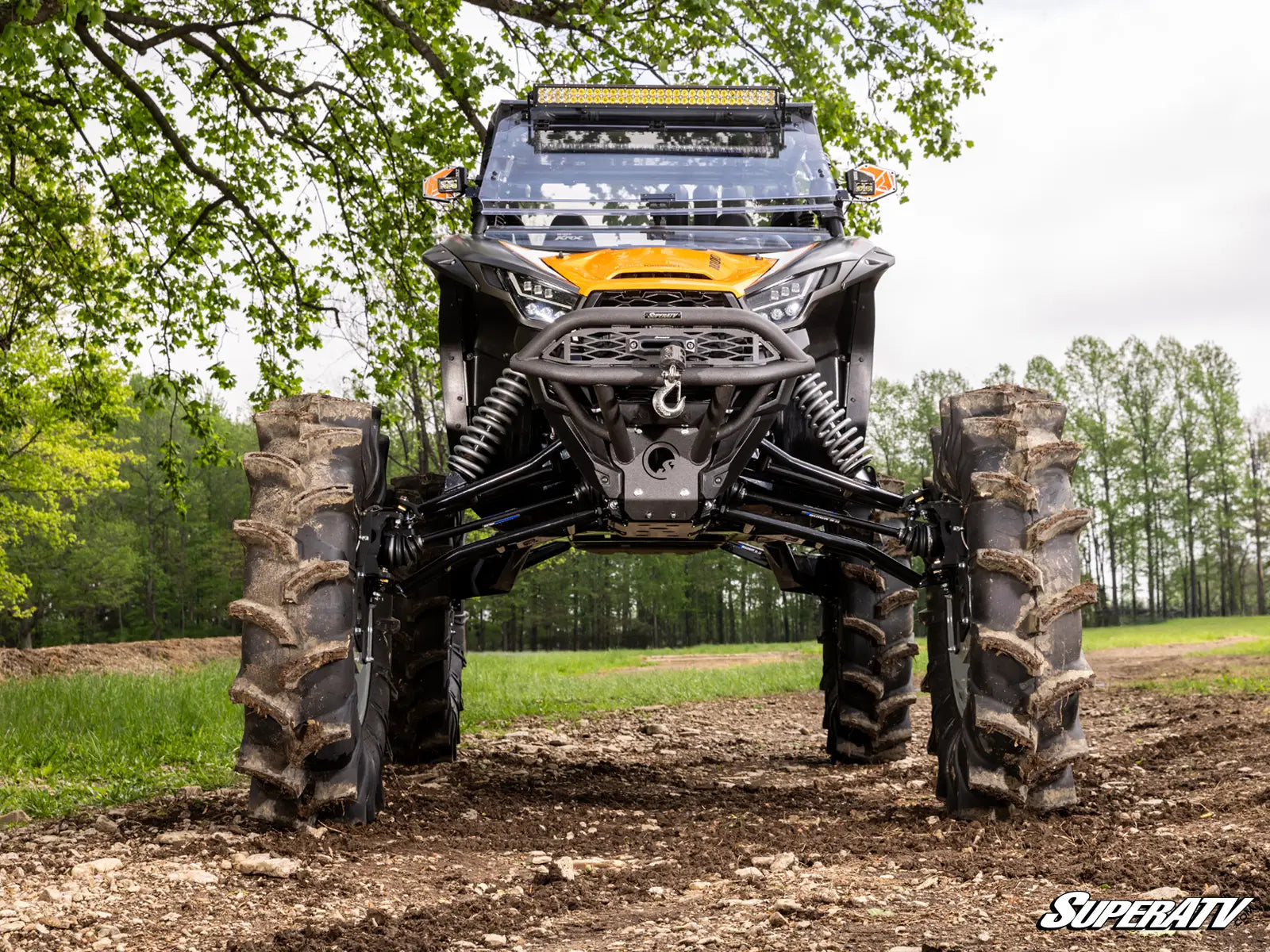Large off-road vehicle with massive tires in a forested area, featuring the SuperATV logo.