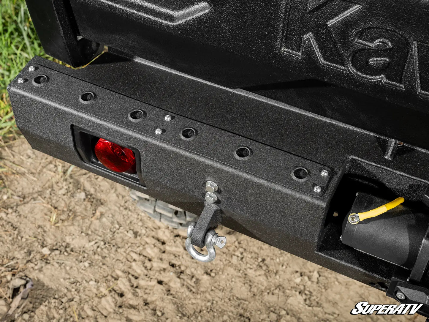 Close-up of a black SuperATV bumper on a vehicle, with grass and dirt in the background.