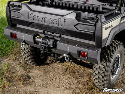 Kawasaki SuperATV vehicle with a focus on the rear bumper and tires on a dirt path.