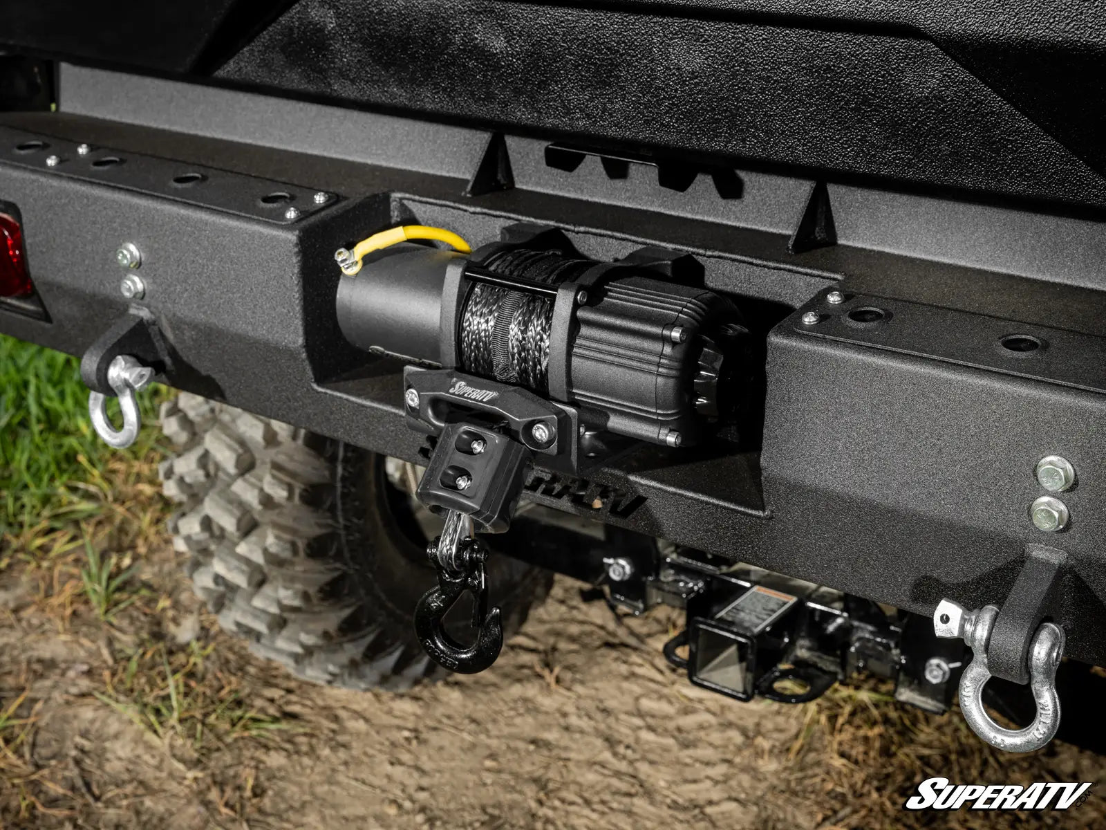 Close-up of a vehicle bumper with towing hooks and lights on a grassy background, featuring the SuperATV logo.