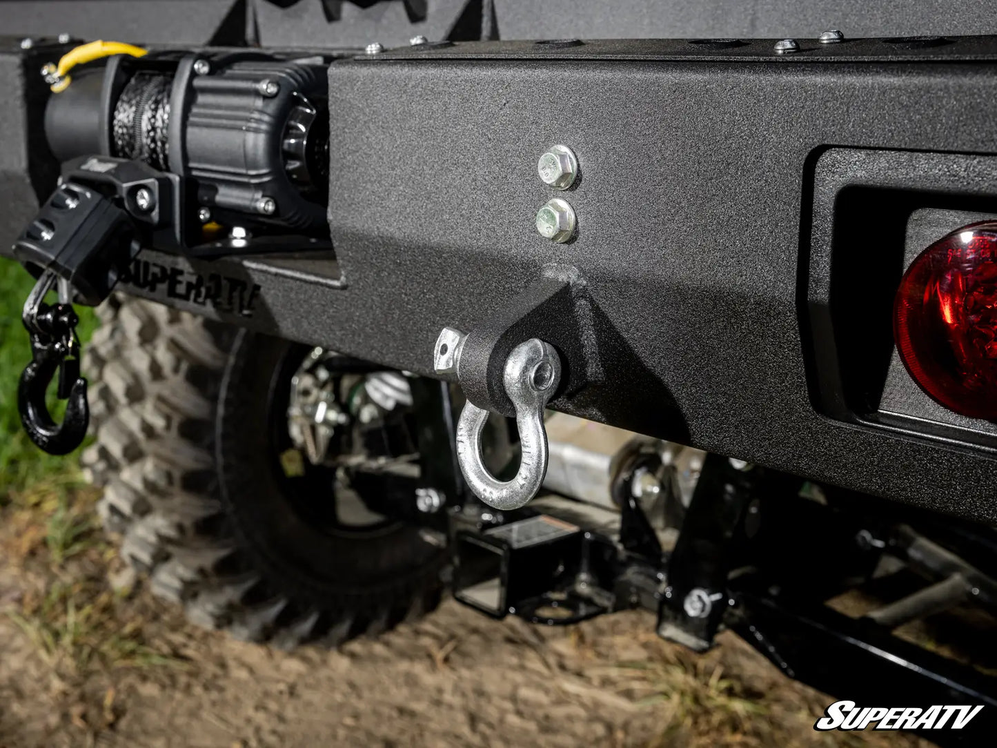 Close-up of a SuperATV vehicle bumper with hooks and lights on a grassy background
