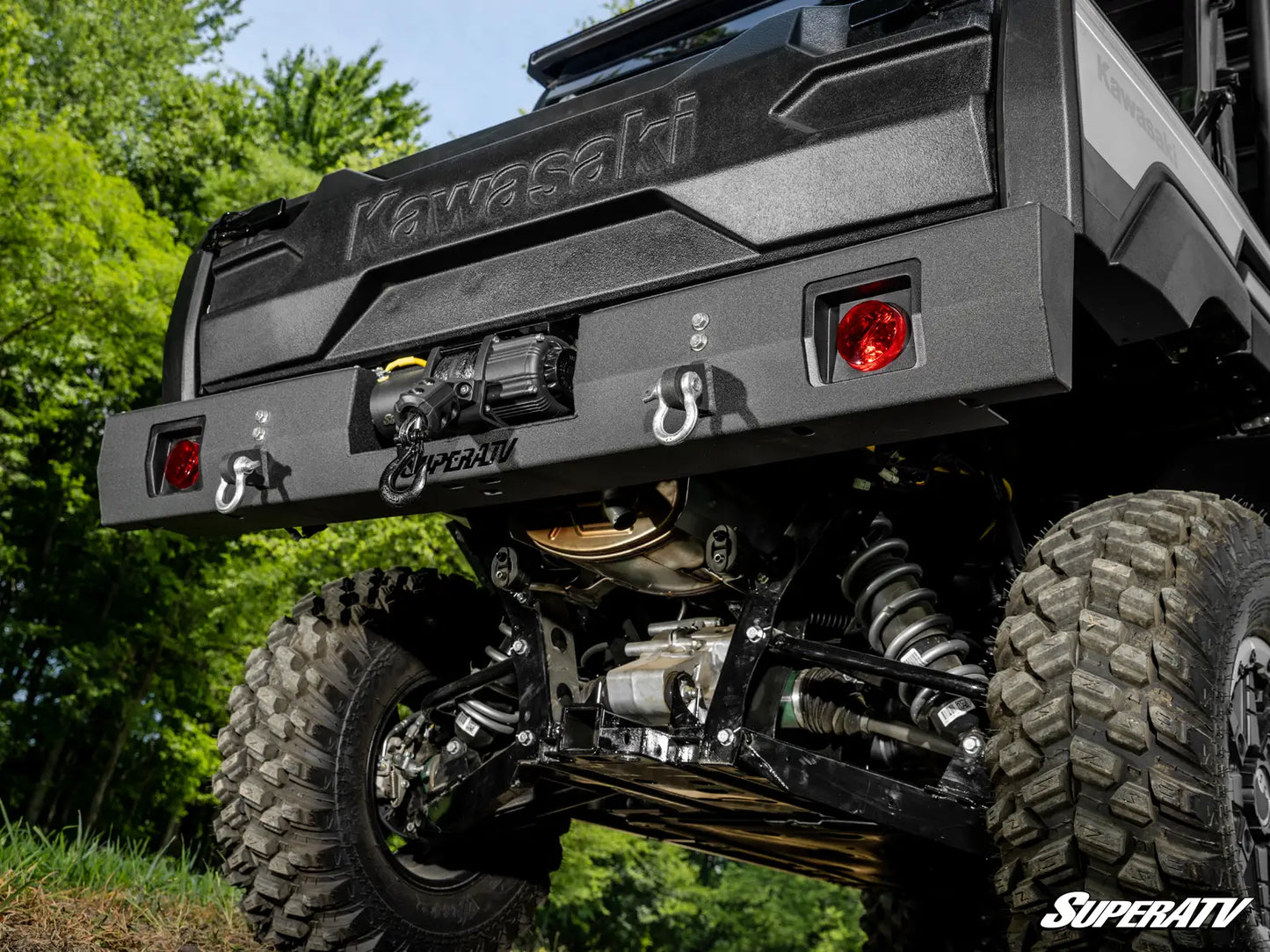 Kawasaki ATV with large off-road tires and SuperATV branding in a natural setting.