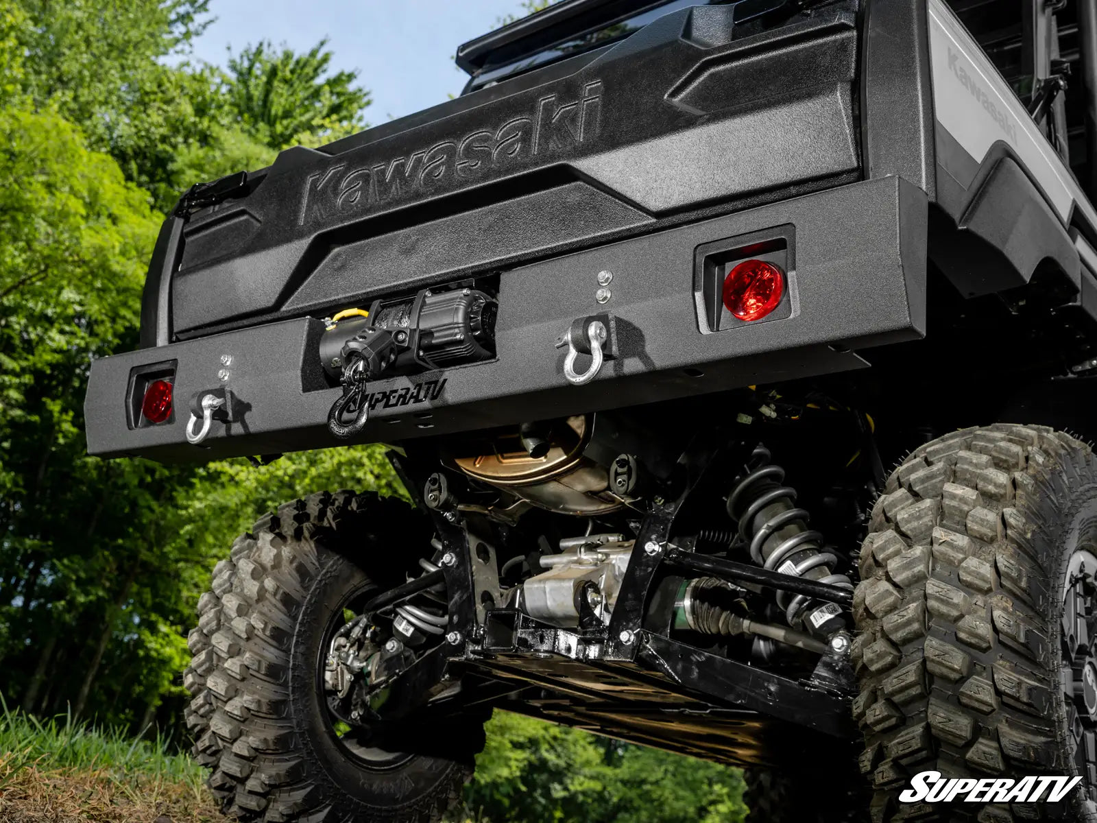 Kawasaki ATV with large off-road tires and SuperATV branding in a natural setting.