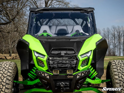 Green and black SuperATV vehicle in an outdoor setting with trees and grass.