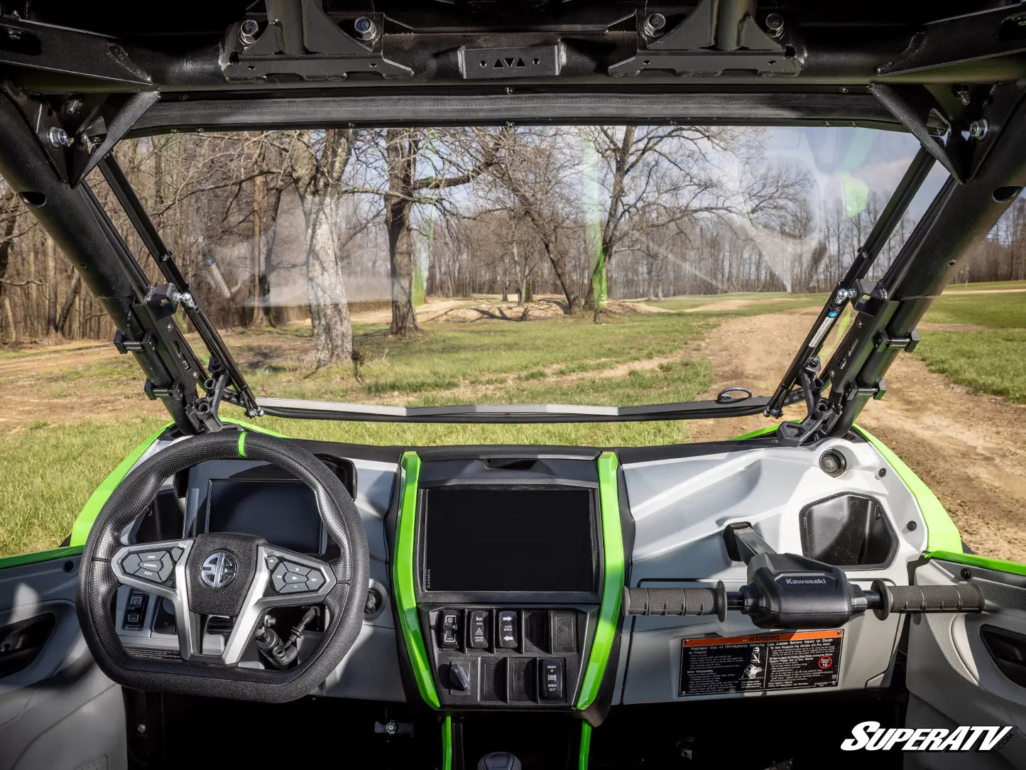 Interior of a SuperATV vehicle with dashboard and steering wheel, showing a forested area outside.