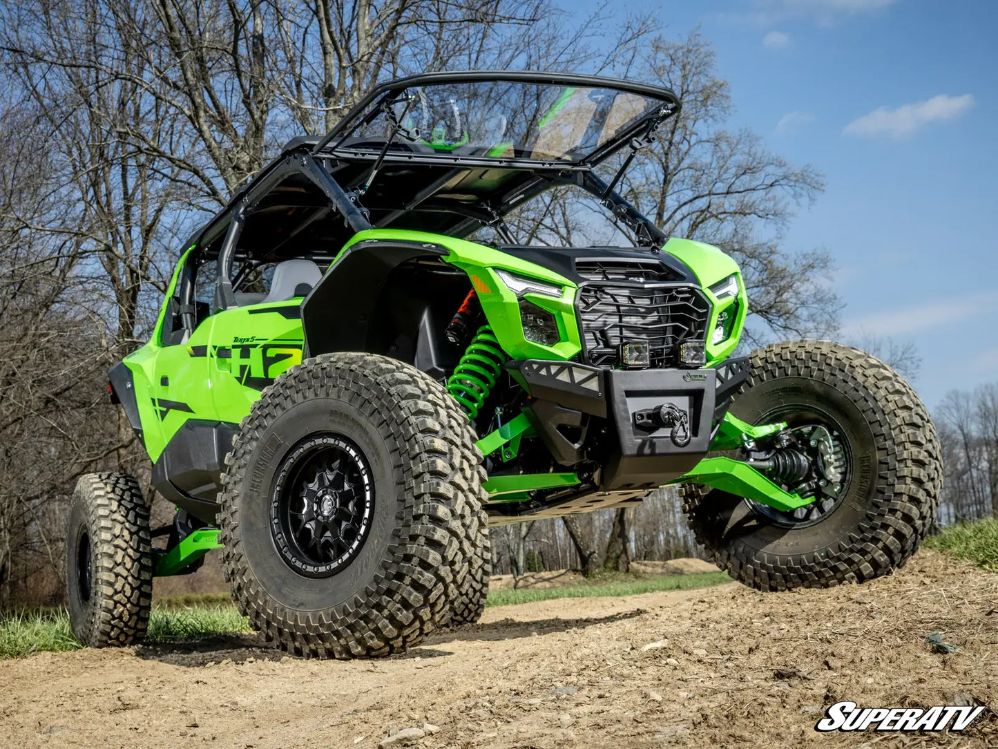 Green off-road vehicle on a dirt path with trees and blue sky in the background