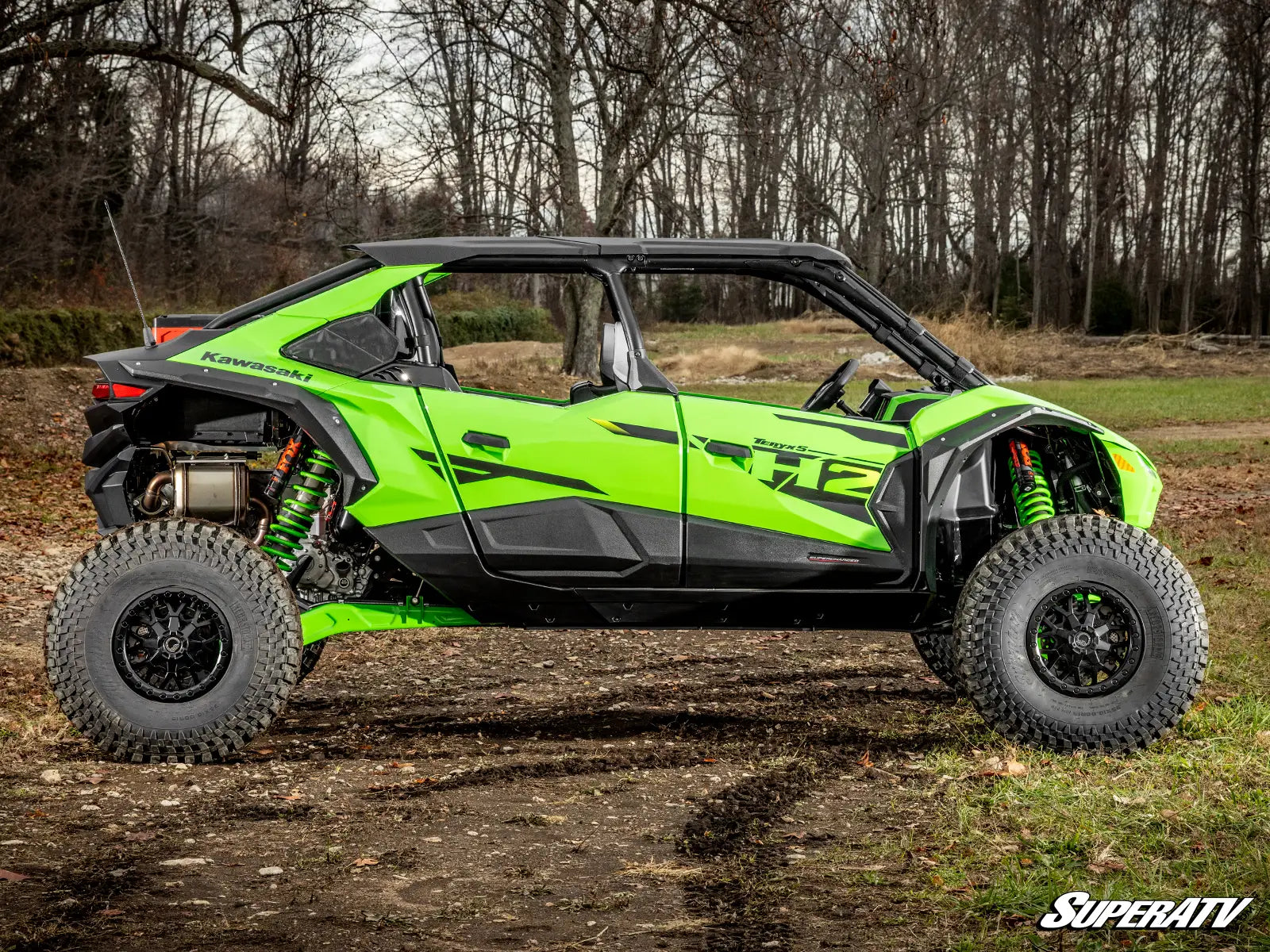 Green and black off-road vehicle on a dirt path with trees in the background