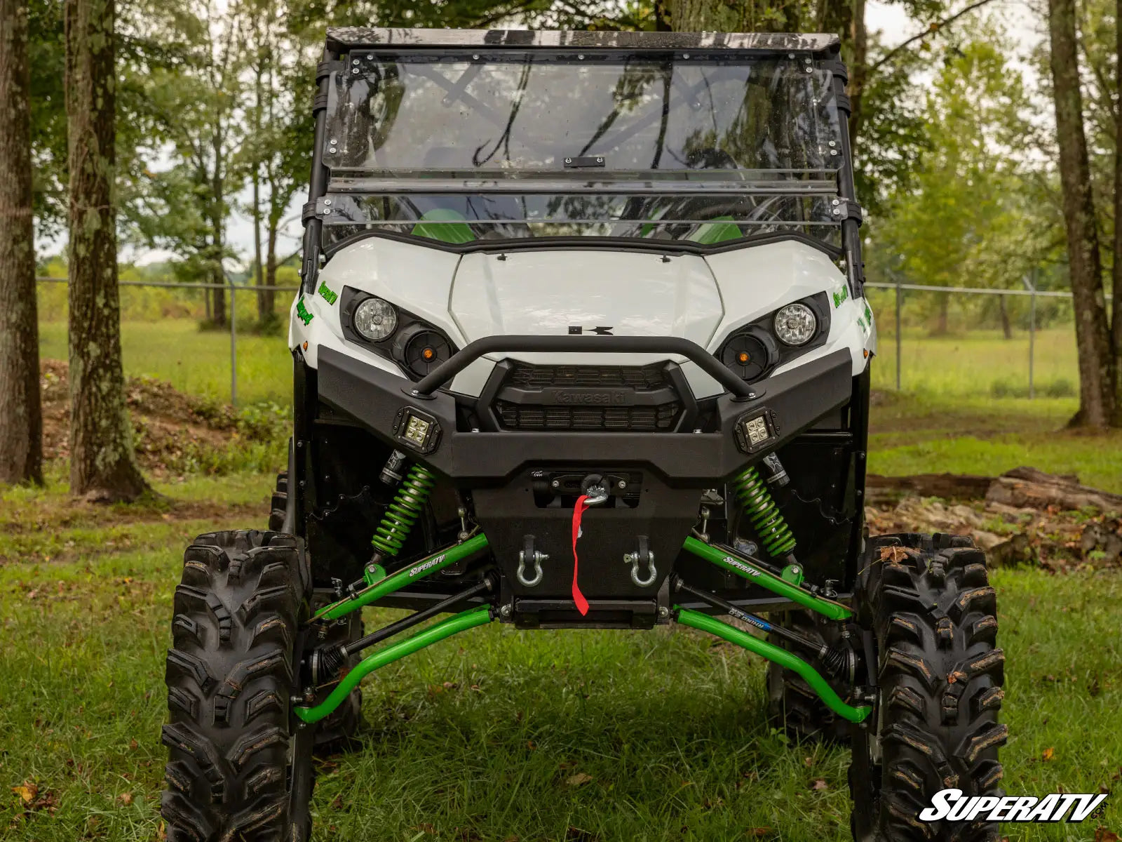 White UTV with green suspension on a grassy area with trees in the background