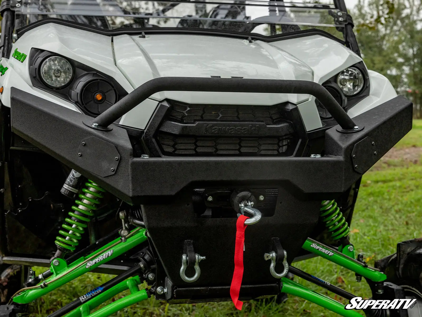 Close-up of a SuperATV vehicle with green suspension and black front bumper on grass.