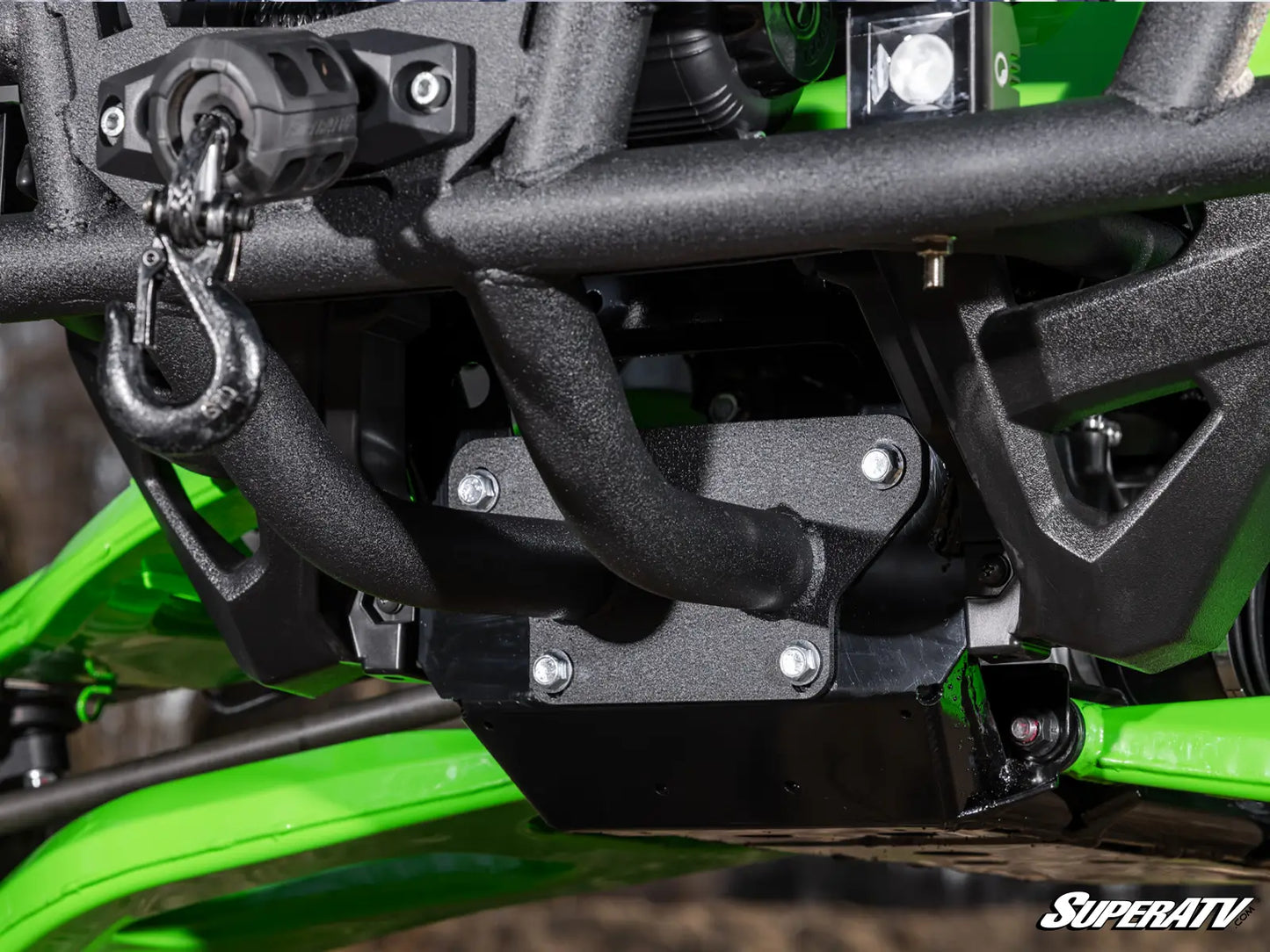 Close-up of a black metal underbarrel winch and mounting bracket attached to a bright green all-terrain vehicle, with a SuperATV logo in the bottom right corner.