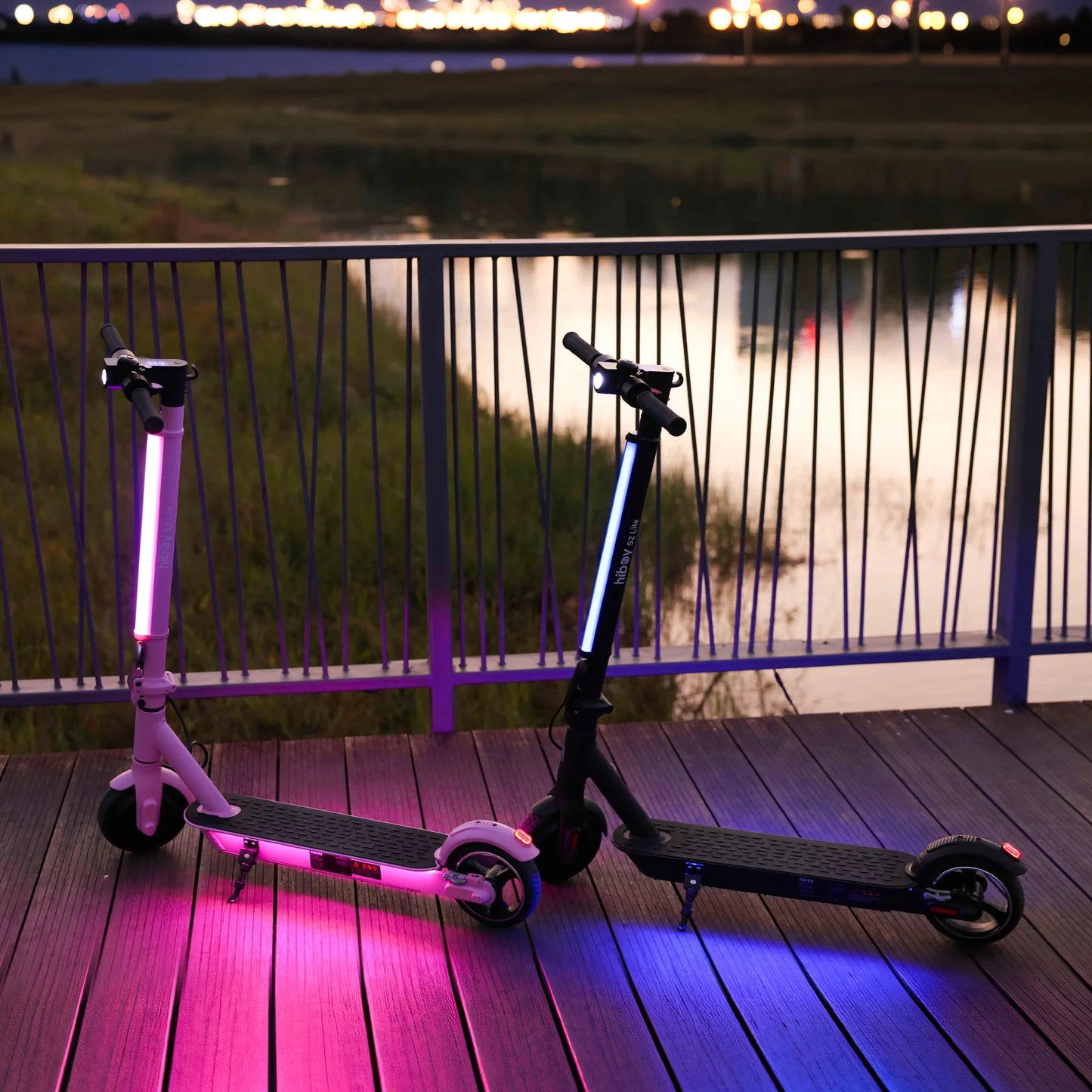 Two electric scooters with LED lights on a wooden deck at night.