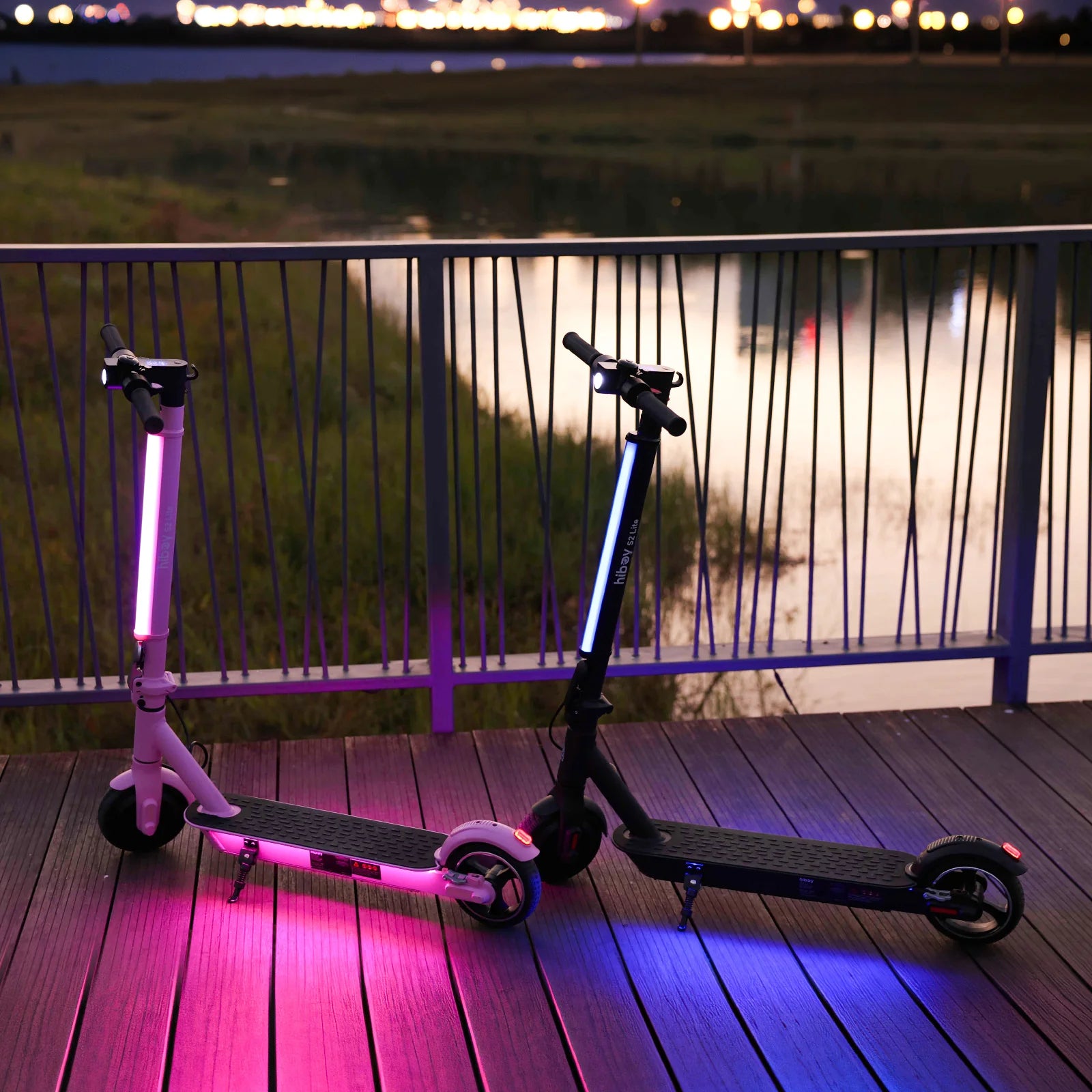 Two electric scooters with LED lights on a wooden deck at night.