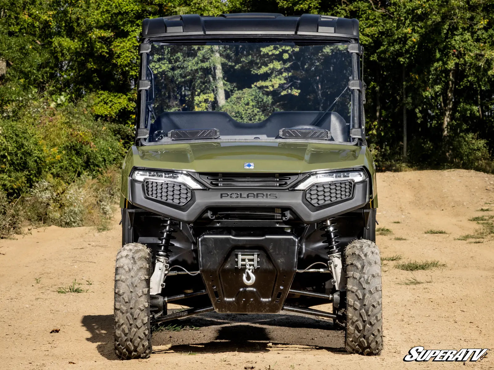 Green Polaris SuperATV vehicle on a dirt road with trees in the background