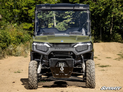 Green Polaris SuperATV vehicle on a dirt road with trees in the background