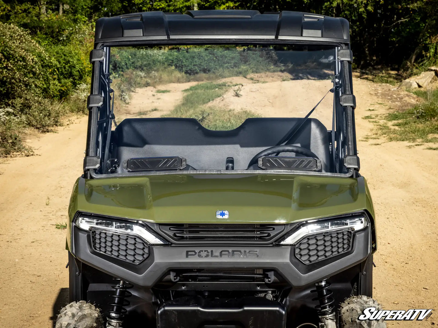 Green Polaris SuperATV vehicle on a dirt path with trees in the background