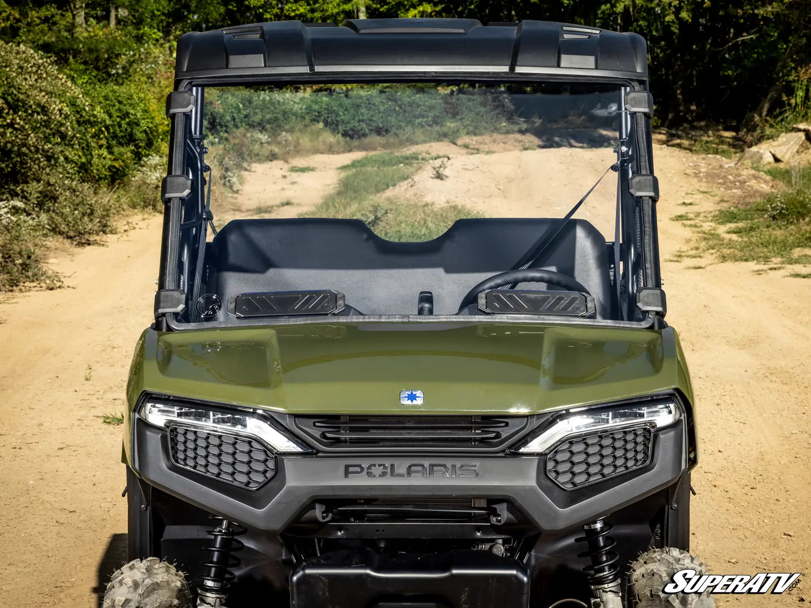 Green Polaris SuperATV vehicle on a dirt path with trees in the background