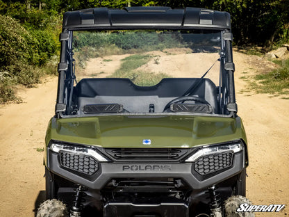 Green Polaris SuperATV vehicle on a dirt path with trees in the background