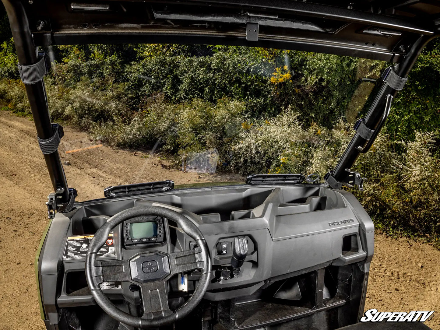 Top view of a SuperATV vehicle interior on a dirt path with greenery.