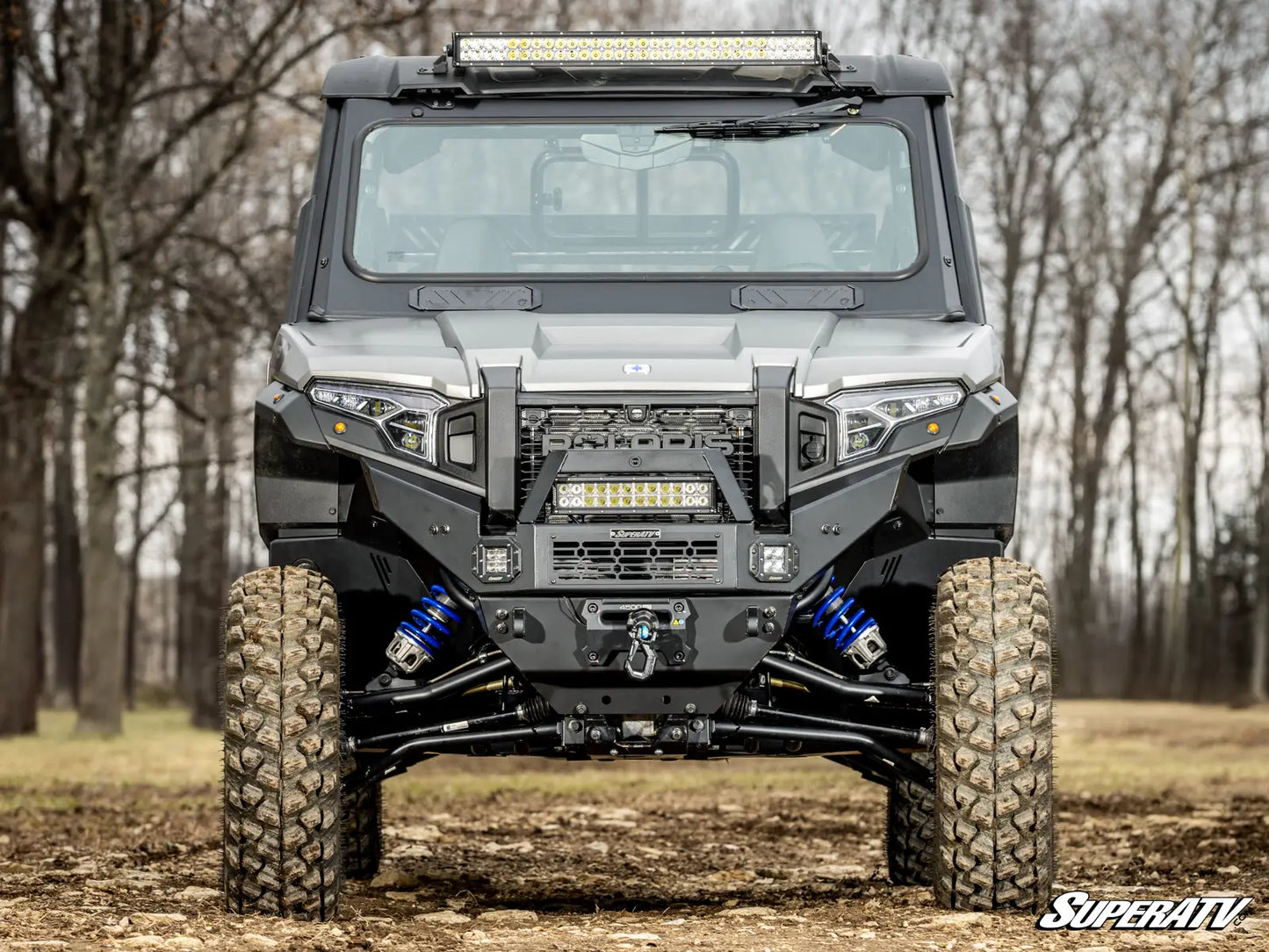 Front view of a large off-road vehicle with 'SuperATV' branding in a forest setting.