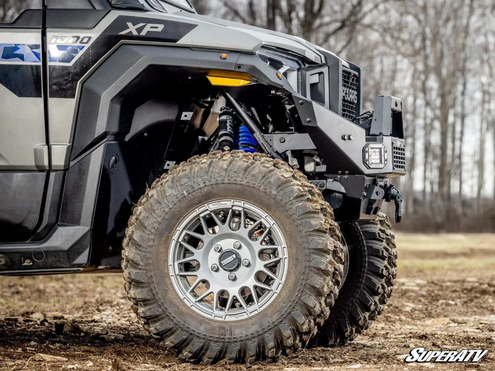 Off-road vehicle with large tires and SuperATV branding in a natural setting.