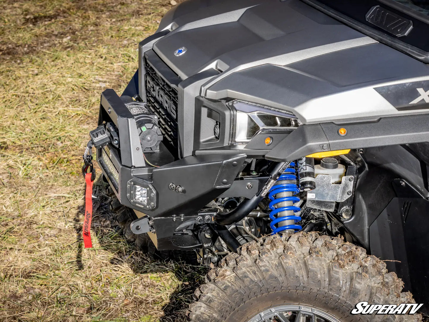 Close-up of an off-road vehicle with suspension system on a grassy surface, featuring SuperATV branding.