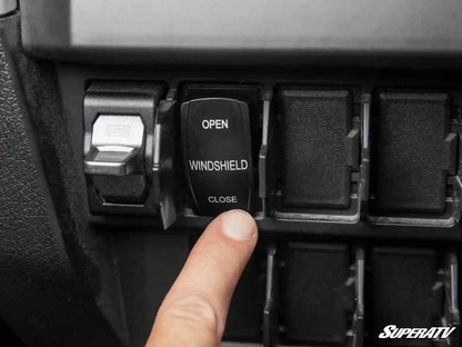 Car window control switch with 'Open Windshield Close' label, finger pressing the switch.