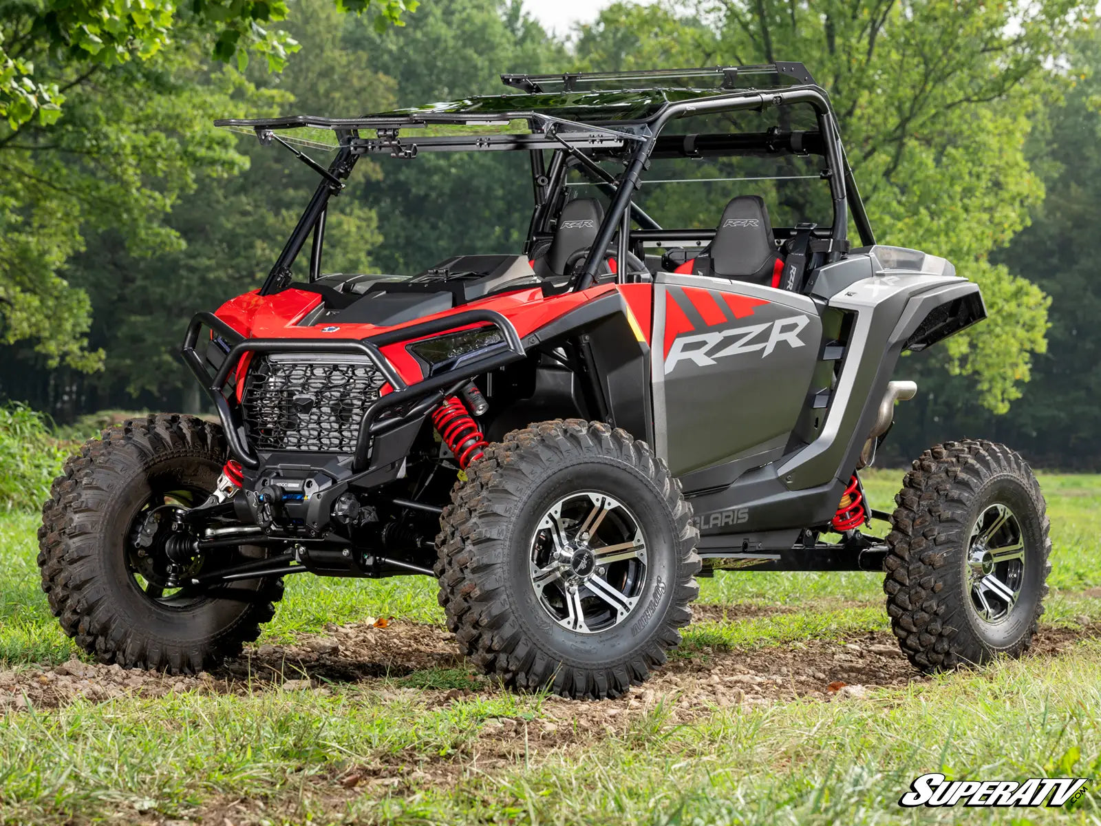 Red and gray RZR vehicle on a grassy field with trees in the background