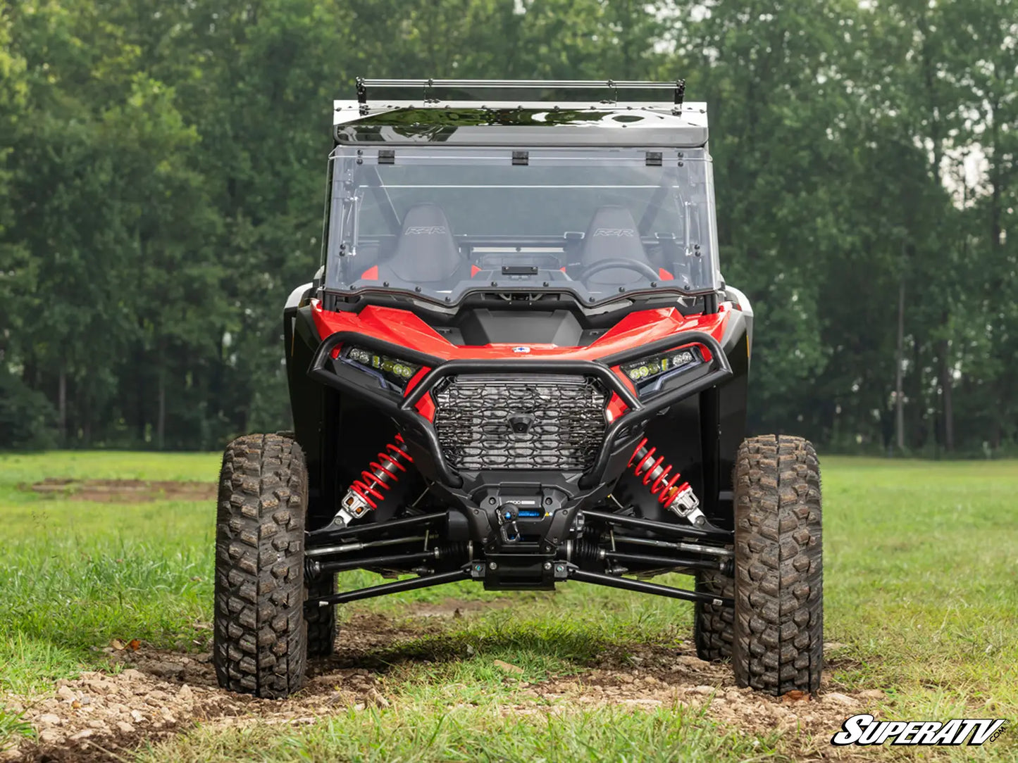 Red and black off-road vehicle in a grassy field with trees in the background