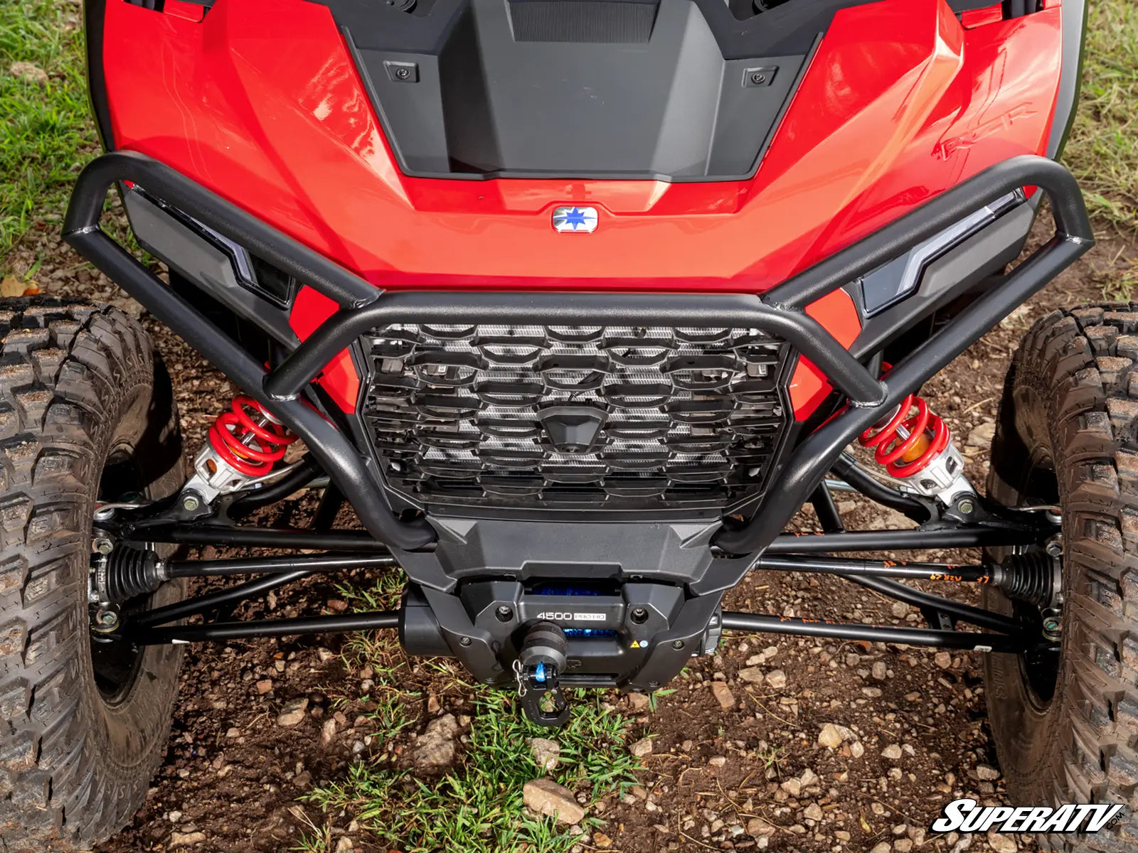 Close-up of a red ATV with a black front bumper on a grassy and rocky terrain.