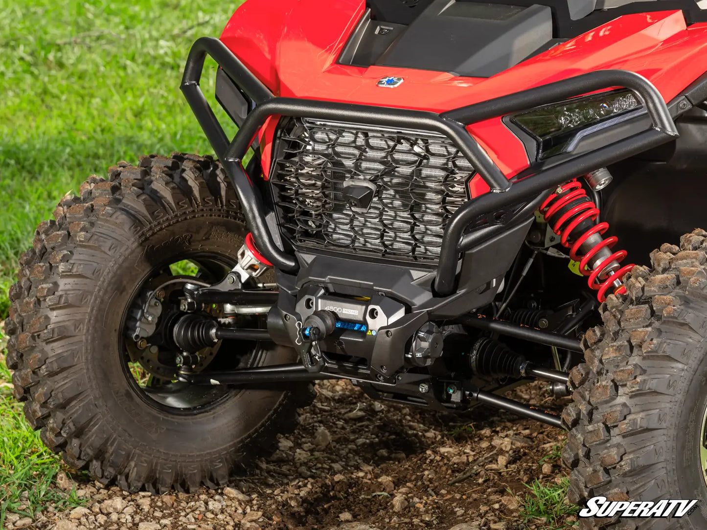 Close-up of a red SuperATV vehicle on a grassy and rocky terrain