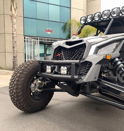 A close-up shot of a gray off-road vehicle with a heavy-duty black front bumper, auxiliary LED lights, and a large knobby tire, parked outdoors in front of a modern glass building.
