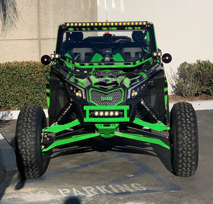A custom-built off-road side-by-side UTV with a striking black and neon green color scheme, parked in a paved parking lot. The vehicle features a roll cage, a front bumper with integrated LED light bars, and oversized knobby tires.