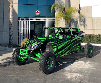 A green and black Can-Am X-Series side-by-side off-road vehicle parked on asphalt in front of a modern building with palm trees.