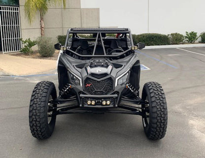 A black Canoo X-Force off-road dune buggy with large knobby tires, a roll cage, and auxiliary lights, parked in an outdoor paved lot.